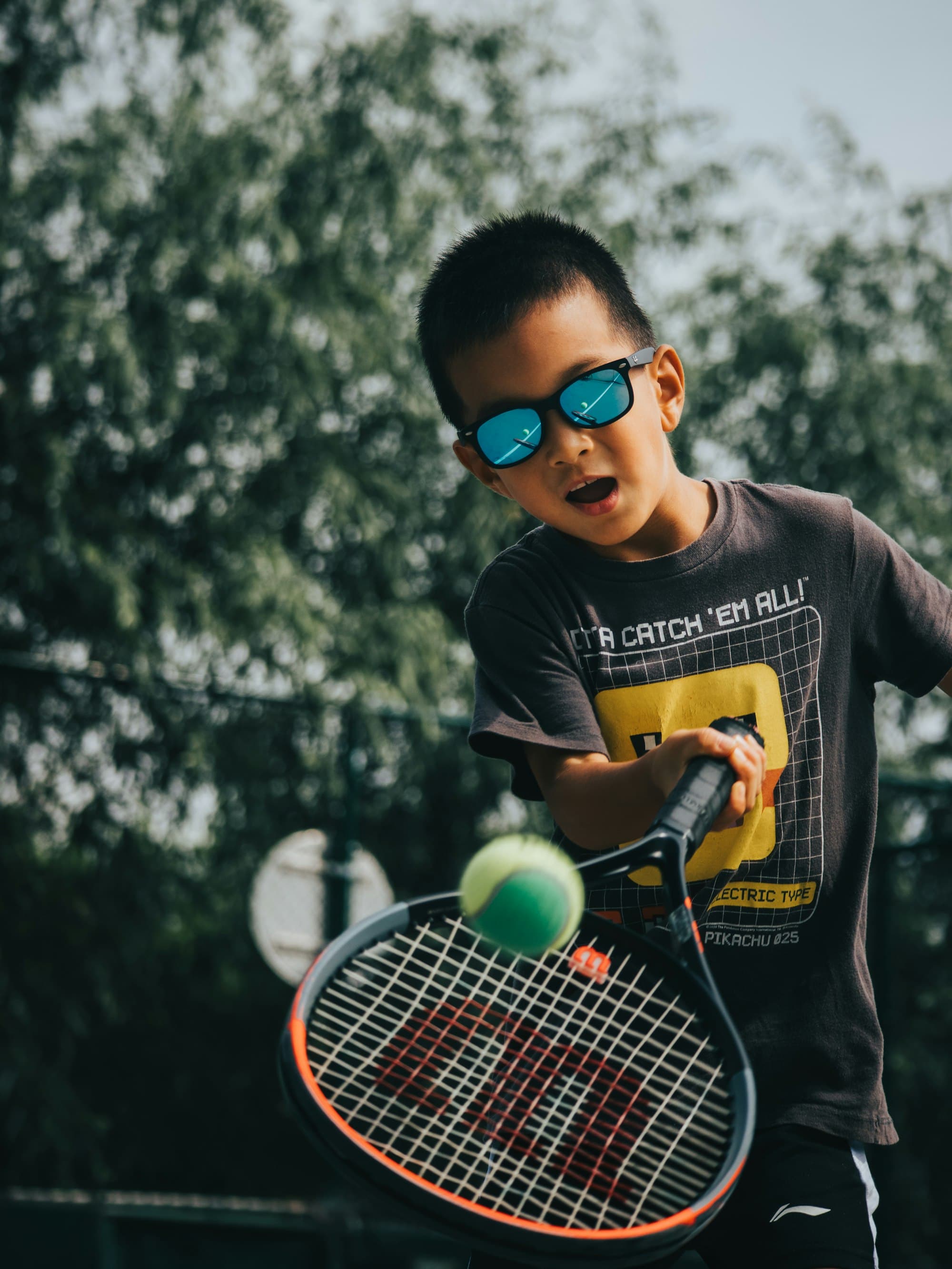 A boy in sunglasses hitting a forehand