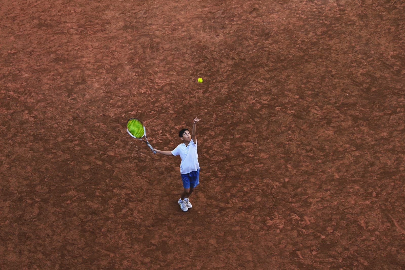A child serving on a clay court, seen from above